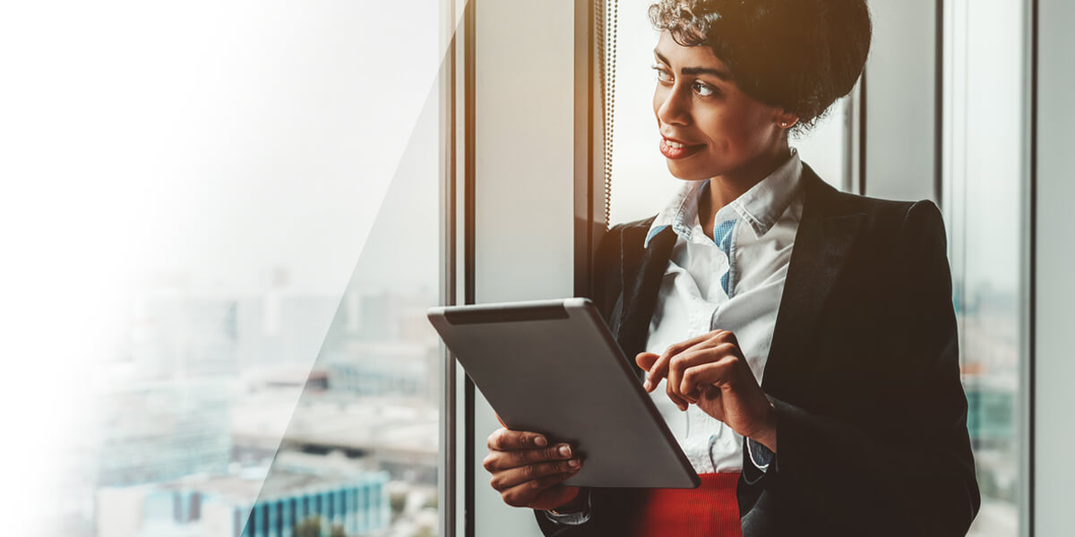 Business woman holding an IPad looking out of office window